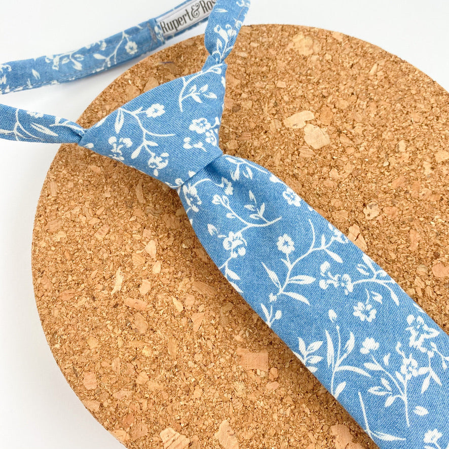 Light denim chambray boys Velcro tie with white floral design, pre-knotted on a matching strap.