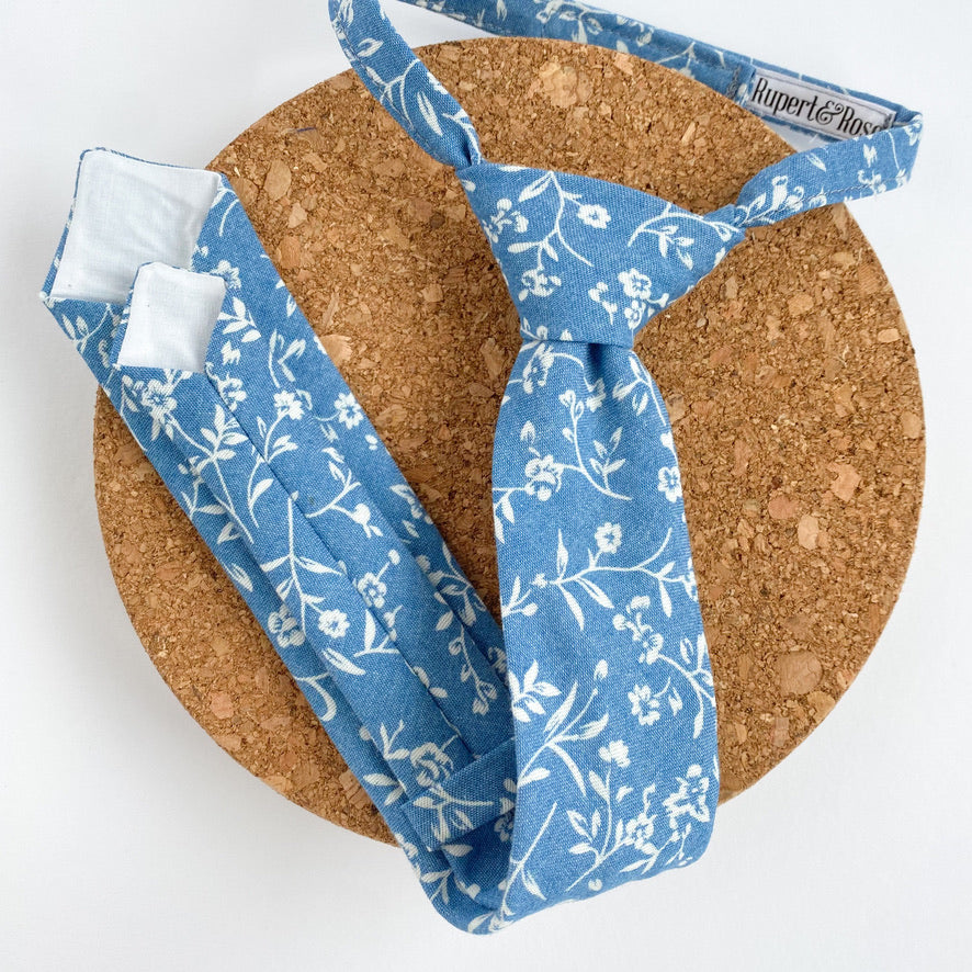 Light denim chambray boys Velcro tie with white floral design, pre-knotted on a matching strap.