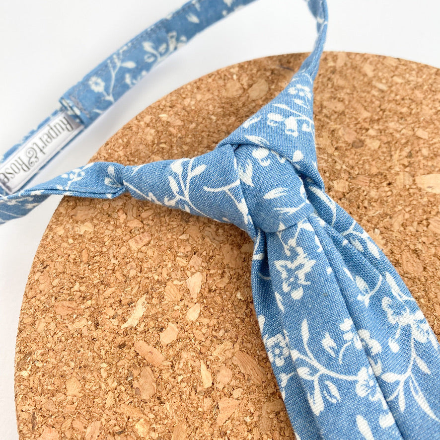 Light denim chambray boys Velcro tie with white floral design, pre-knotted on a matching strap.