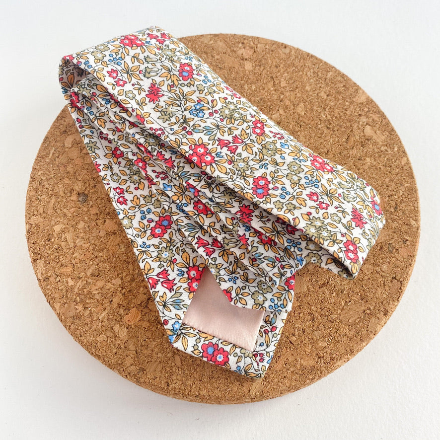 RUBEN Boys Self Tie featuring a floral pattern in sage green, cornflower blue, yellow, and vibrant pink on an off-white background.