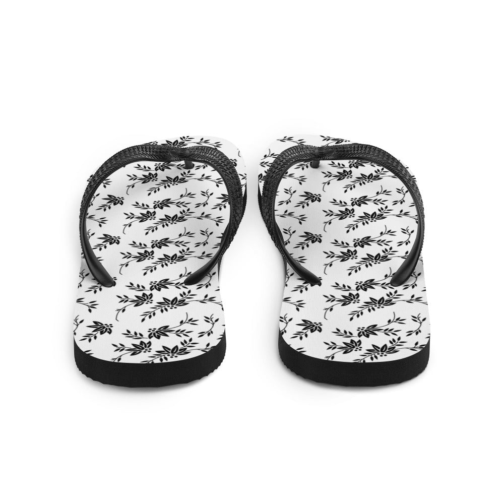 A pair of stylish Black and White Floral Flip-Flops featuring a rubber sole, soft fabric lining, and black Y-shaped straps, perfect for summer wear.