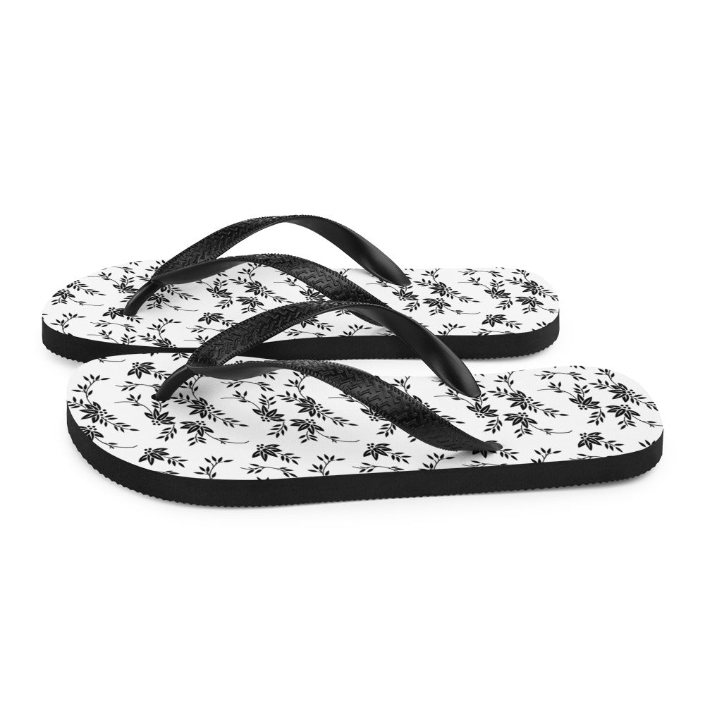 A pair of stylish Black and White Floral Flip-Flops featuring a rubber sole, soft fabric lining, and black Y-shaped straps, perfect for summer wear.