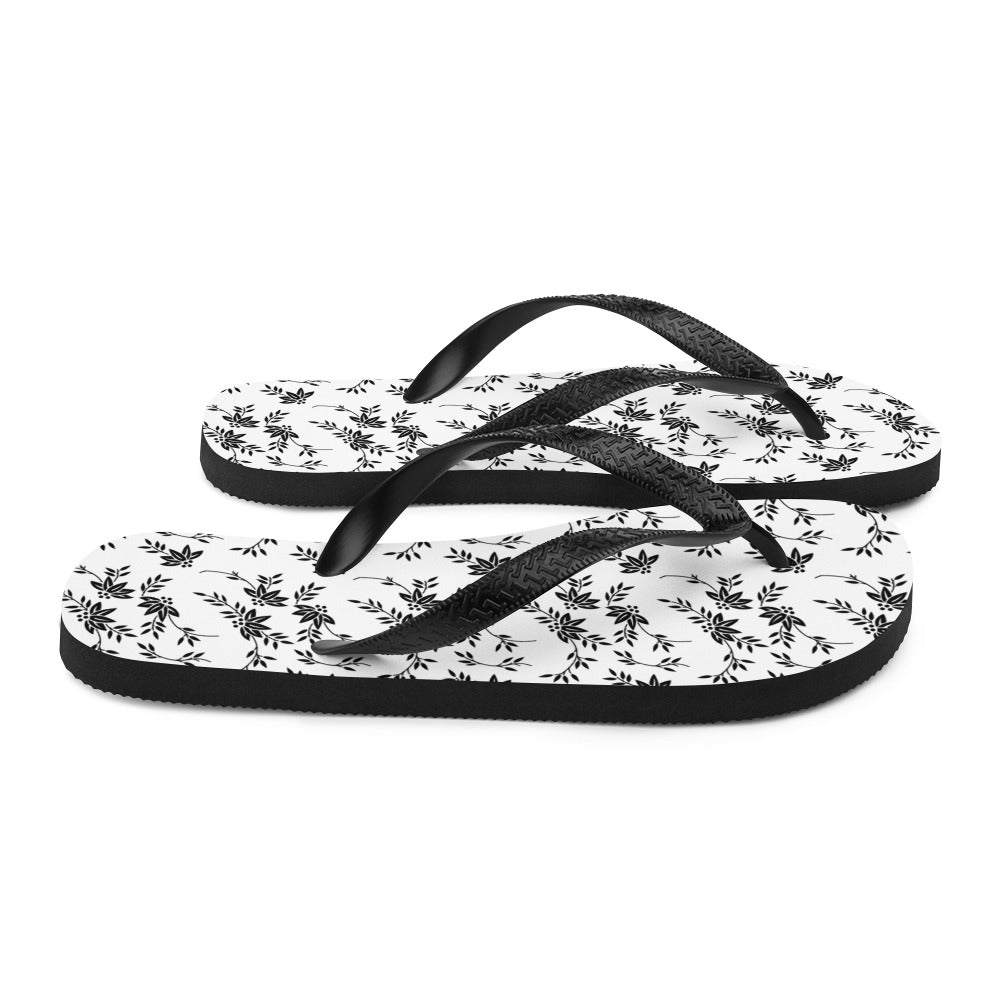 A pair of stylish Black and White Floral Flip-Flops featuring a rubber sole, soft fabric lining, and black Y-shaped straps, perfect for summer wear.