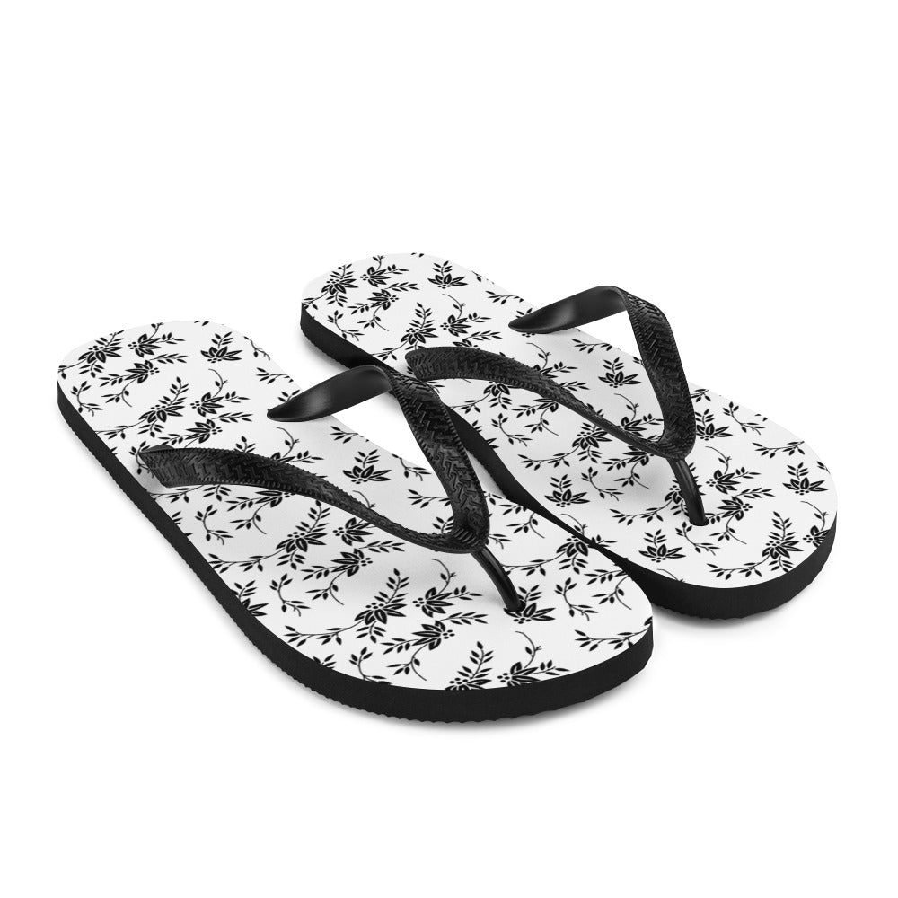 A pair of stylish Black and White Floral Flip-Flops featuring a rubber sole, soft fabric lining, and black Y-shaped straps, perfect for summer wear.