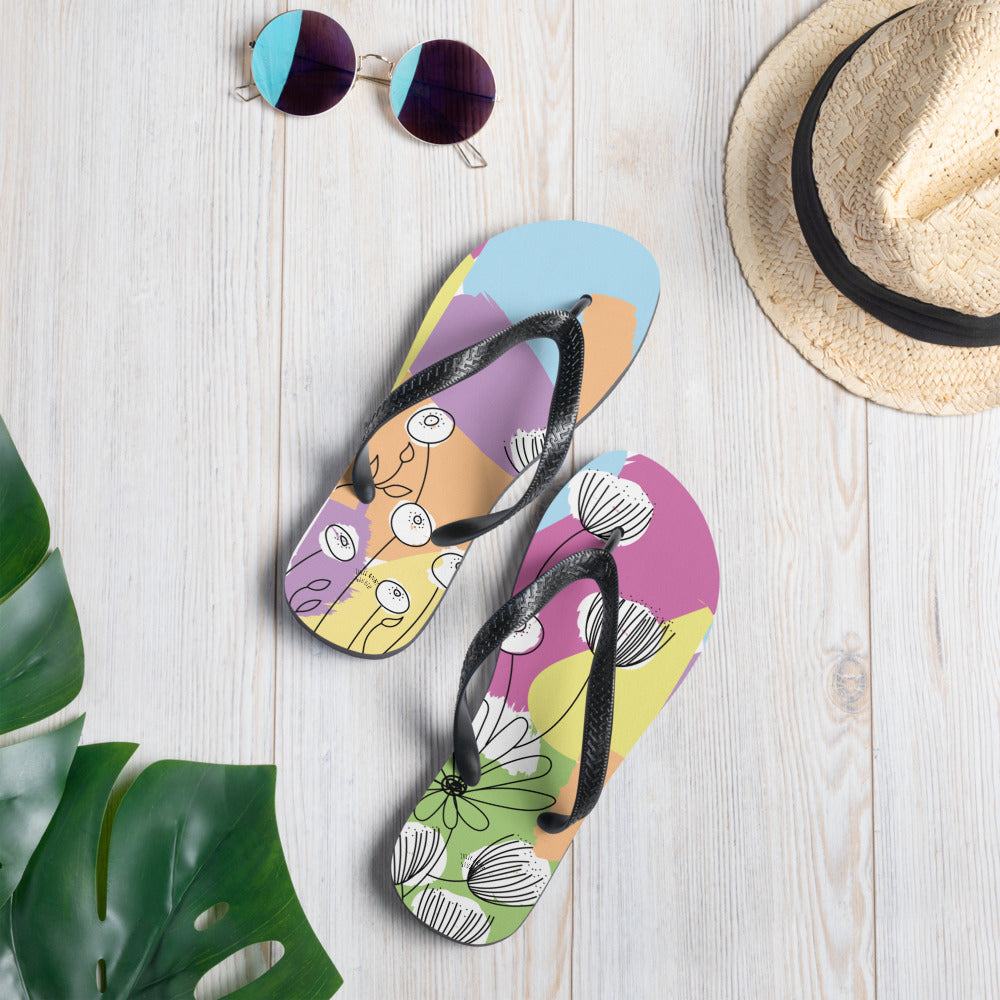 A pair of Pretty Pastel Flower Print Flip-Flops featuring a vibrant floral design, black rubber straps, and a soft fabric lining, perfect for summer wear.