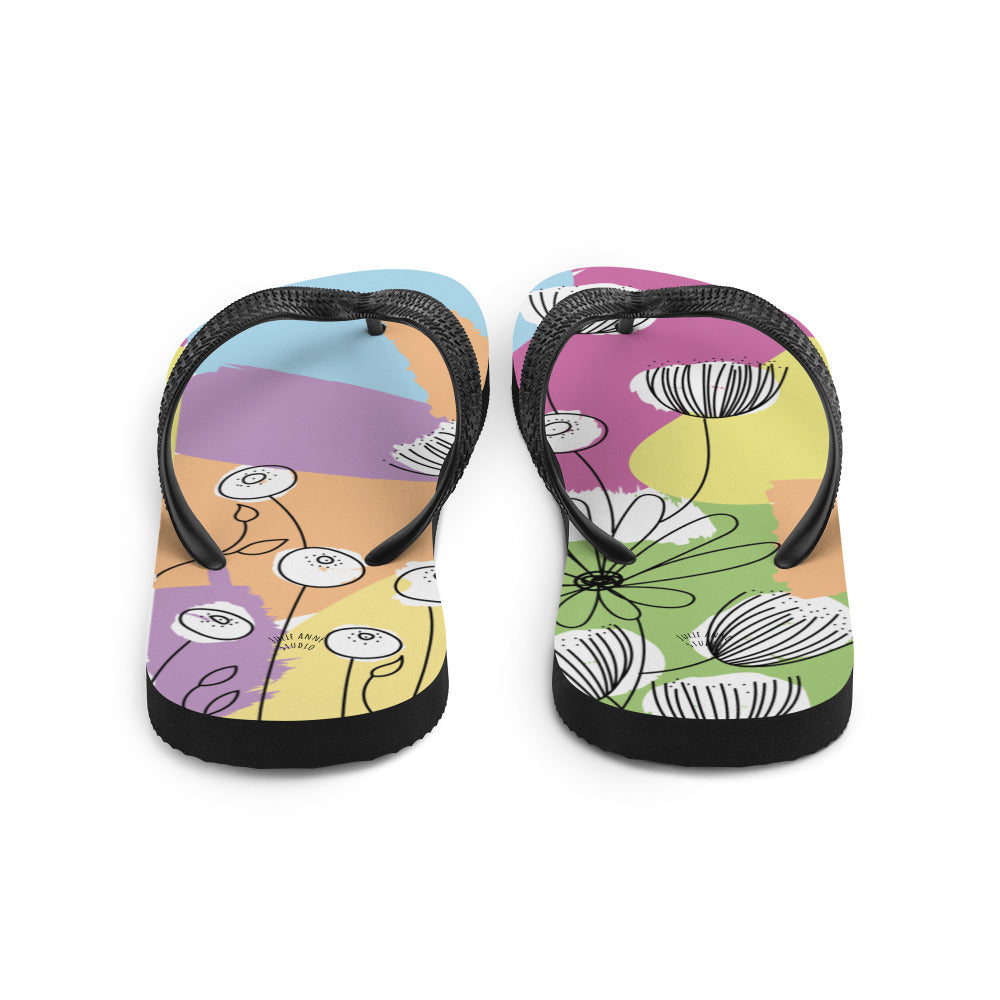 A pair of Pretty Pastel Flower Print Flip-Flops featuring a vibrant floral design, black rubber straps, and a soft fabric lining, perfect for summer wear.