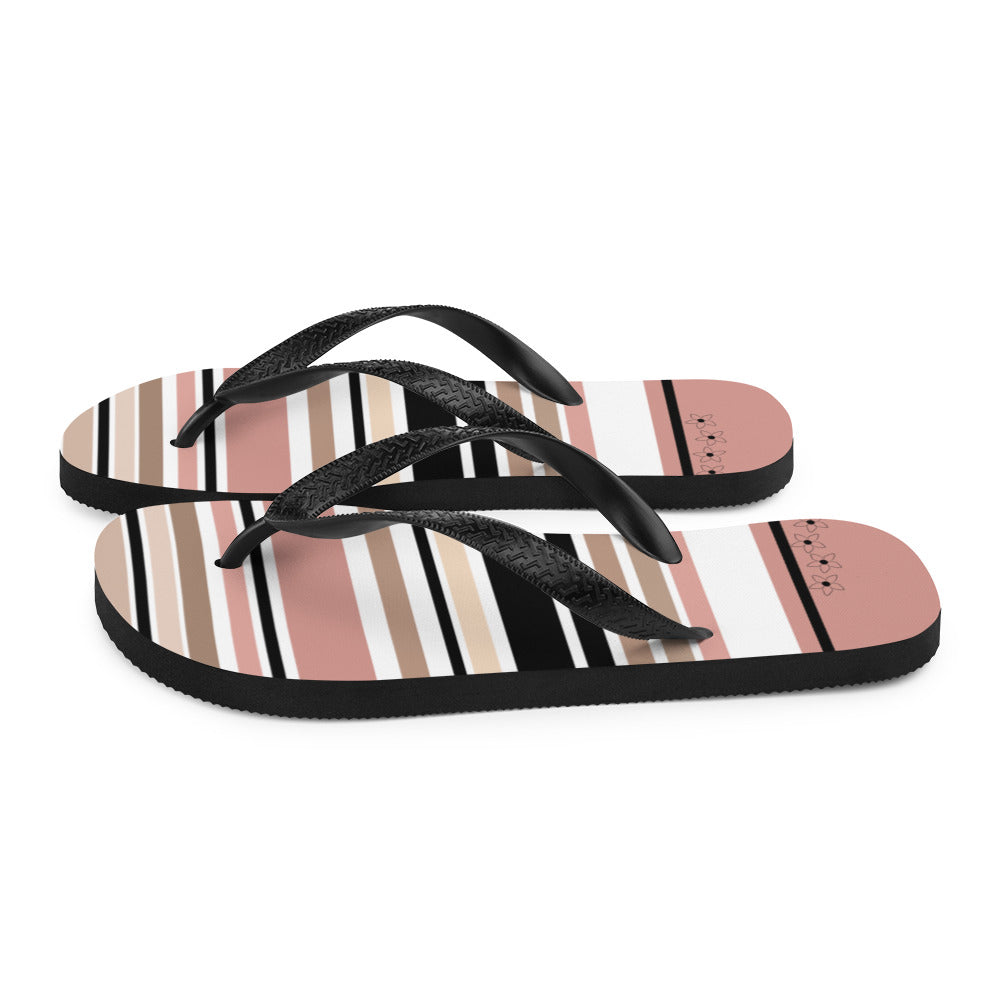 Striped beige, black, and cream flip flops with flower detail, featuring black rubber straps and a soft fabric lining, perfect for summer beach outings.