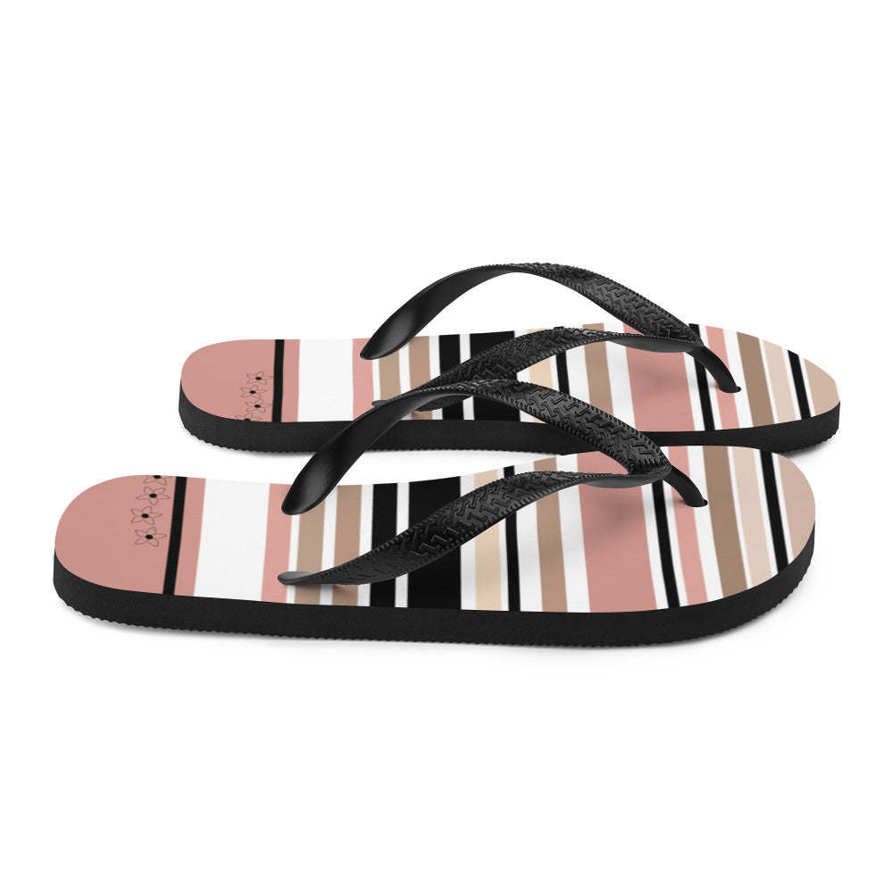 Striped beige, black, and cream flip flops with flower detail, featuring black rubber straps and a soft fabric lining, perfect for summer beach outings.