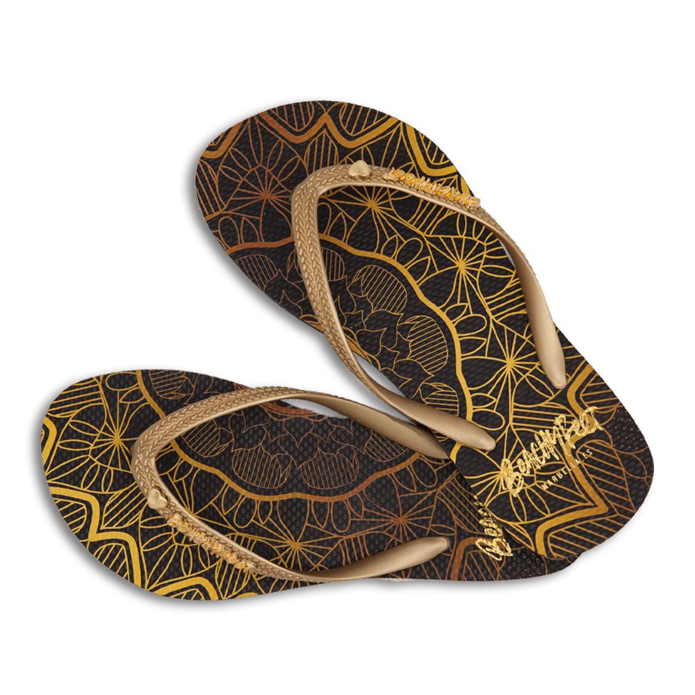 BeachyFeet® Mandala flip flops featuring a black and gold bohemian print with an orange strap and golden emblem.