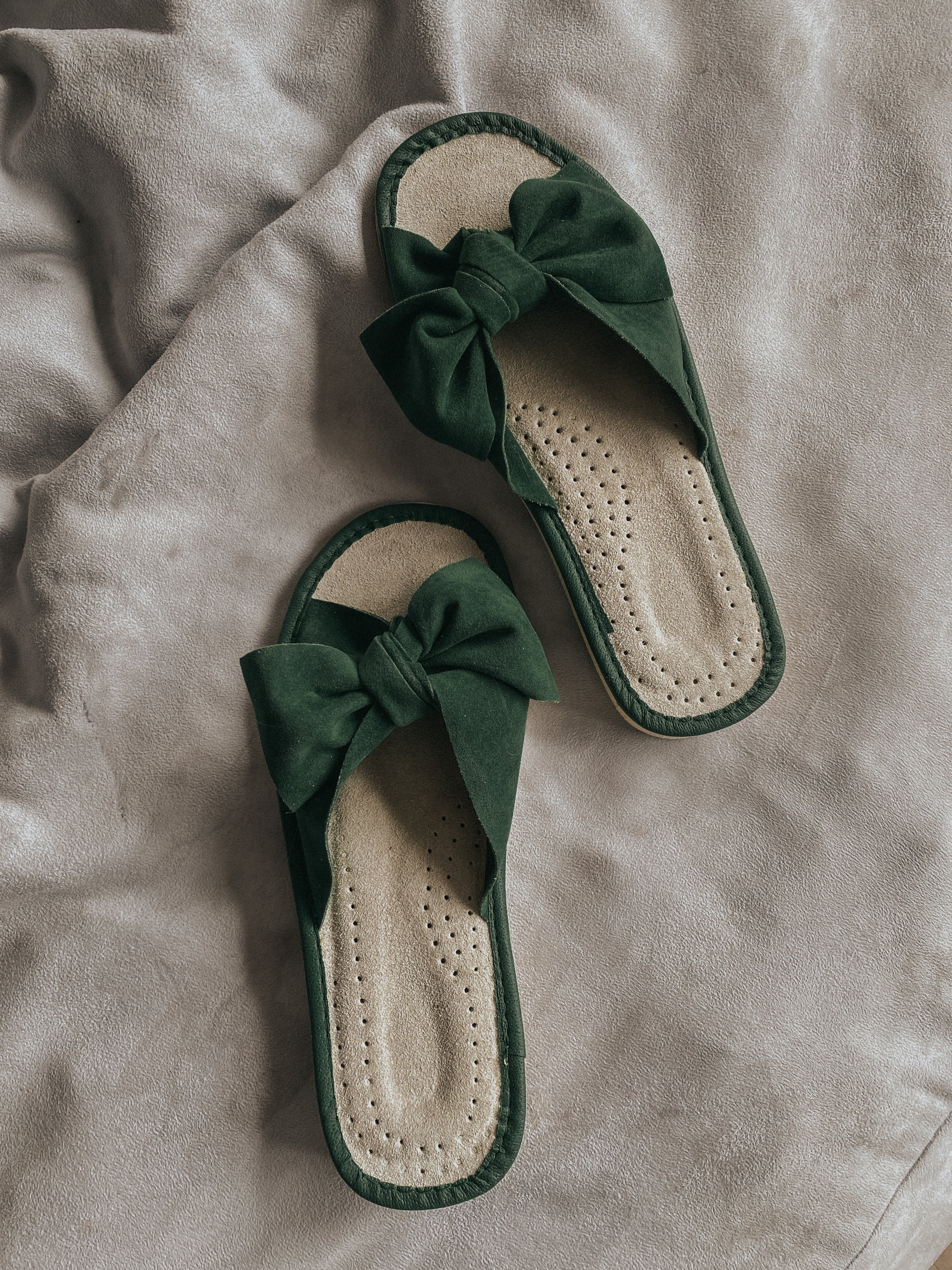 Stylish green suede slippers with a decorative ribbon front and cushioned insole, perfect for home wear.