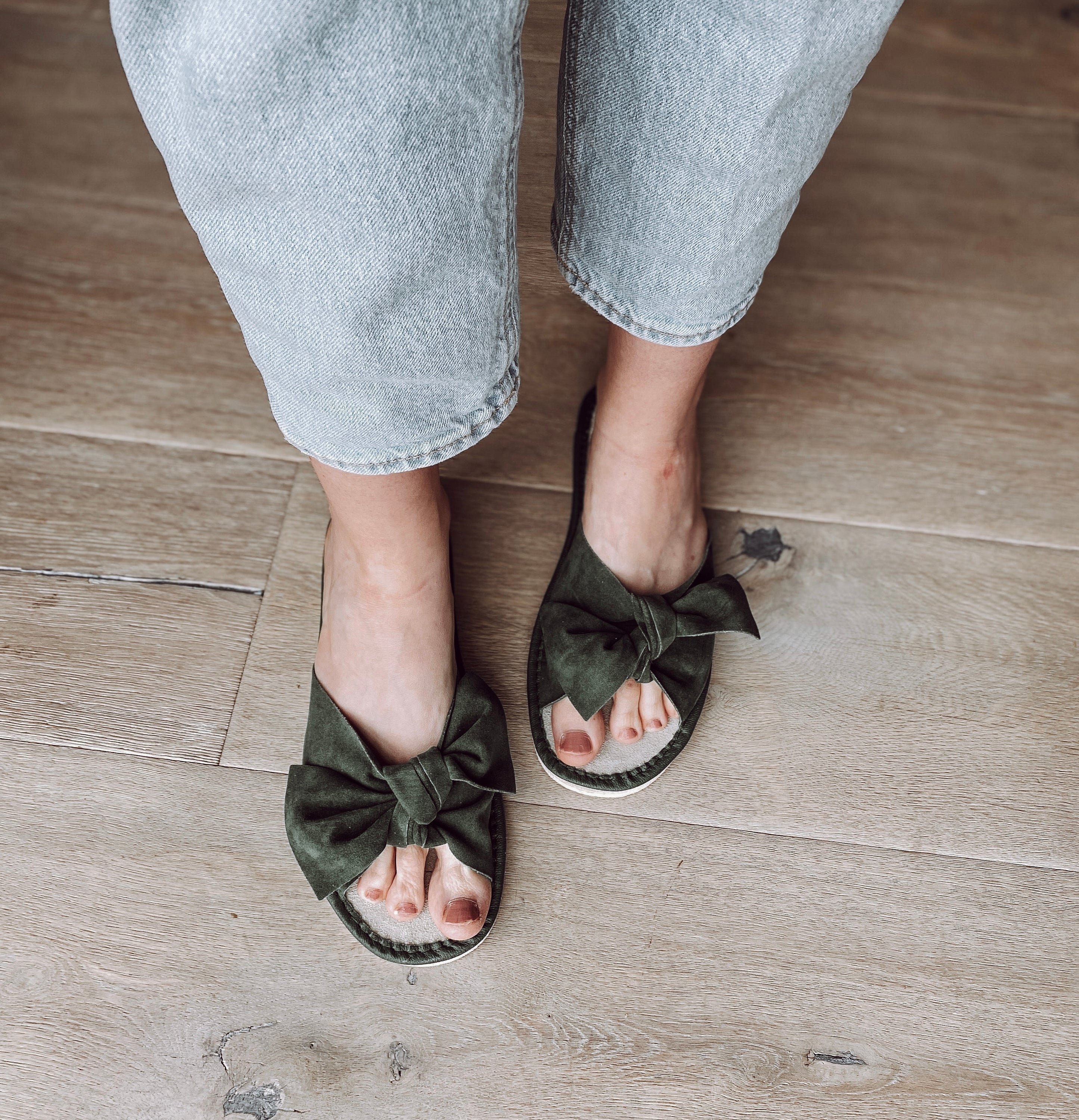 Stylish green suede slippers with a decorative ribbon front and cushioned insole, perfect for home wear.