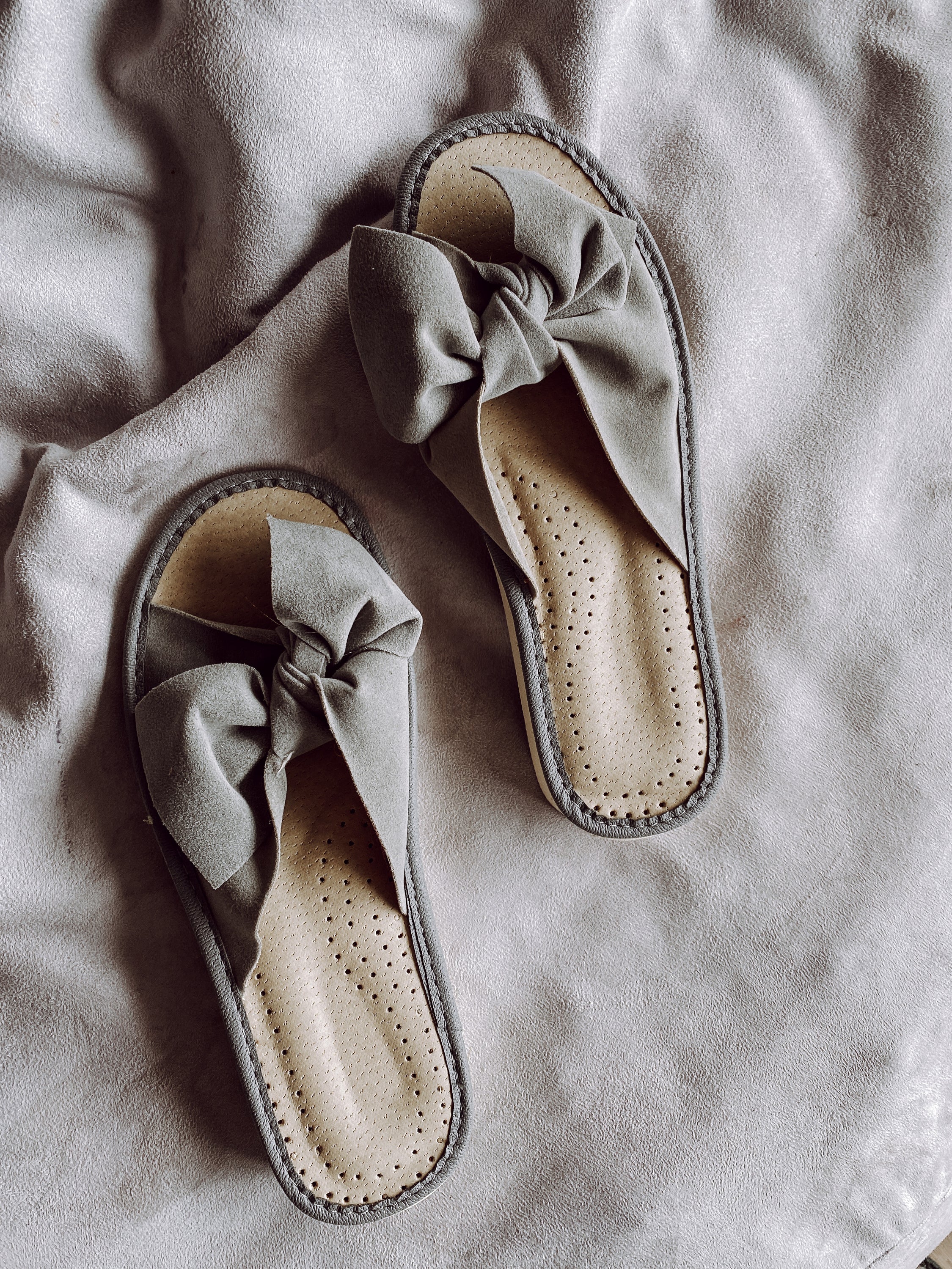 Stylish grey suede slippers with a decorative ribbon front and cushioned insole, perfect for home wear.