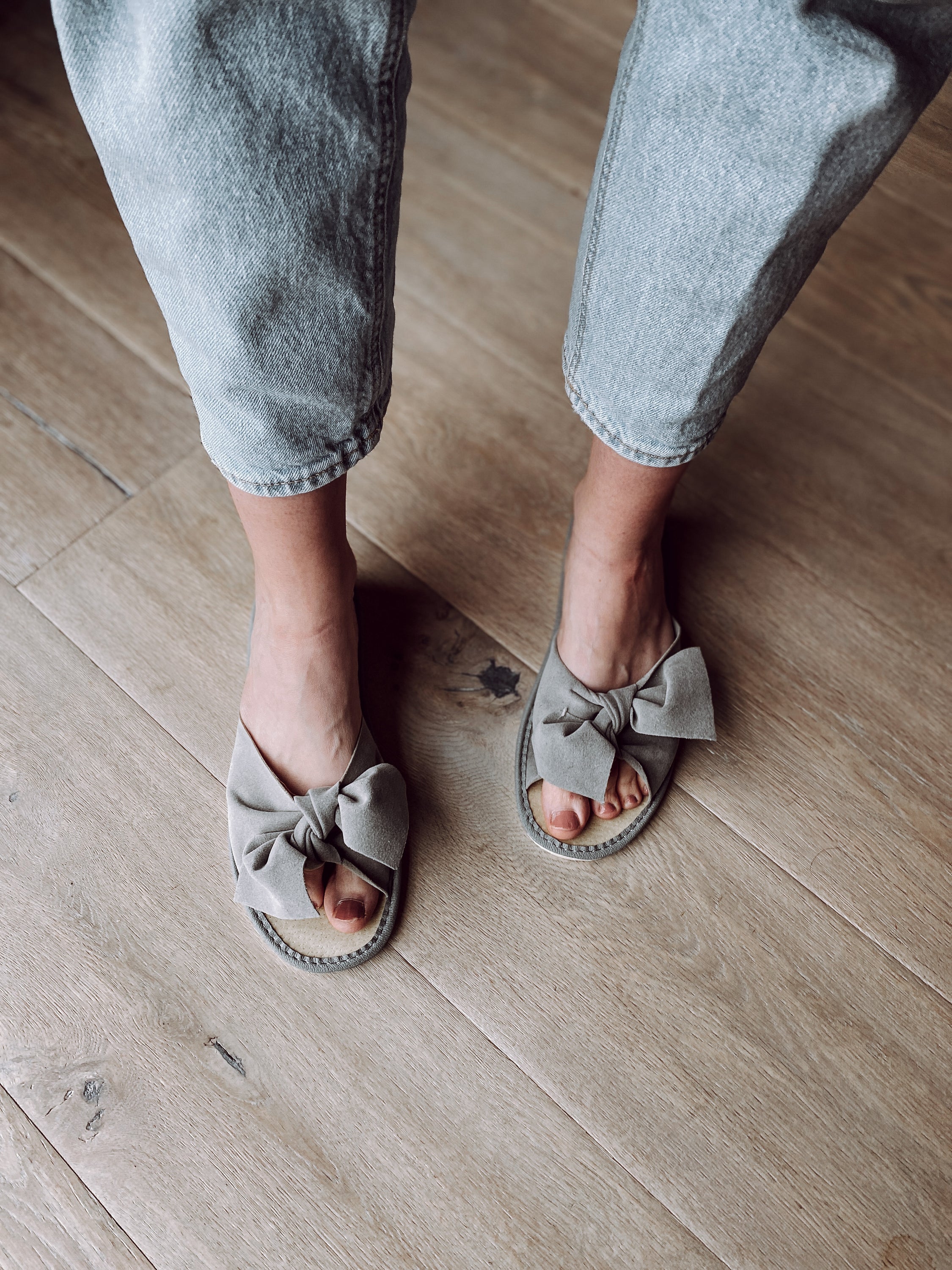 Stylish grey suede slippers with a decorative ribbon front and cushioned insole, perfect for home wear.