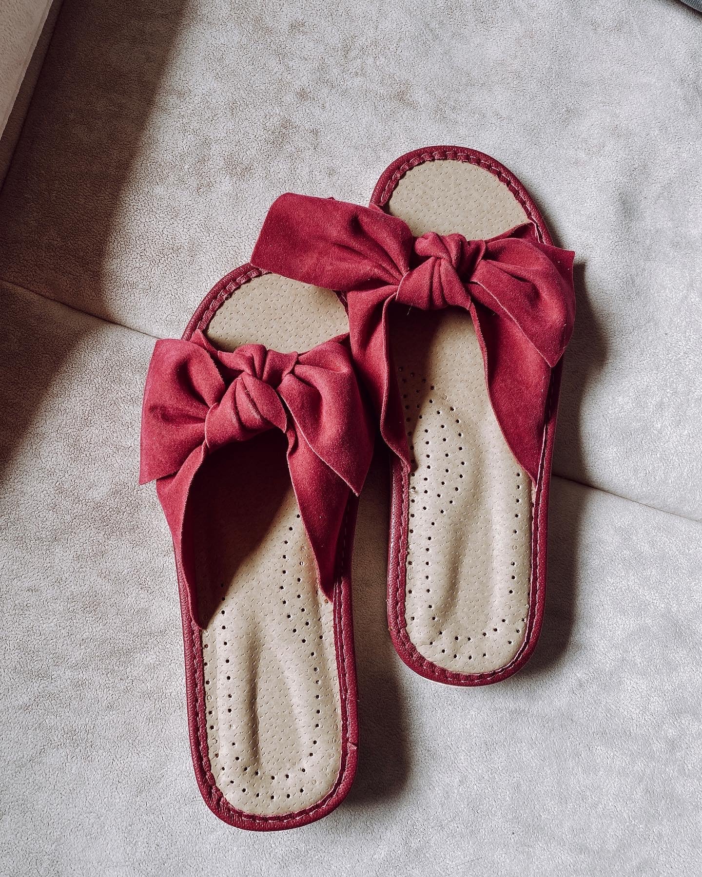 A pair of pink suede slippers featuring a decorative ribbon on the front, designed for comfort with a cushioned insole and foam bottom.