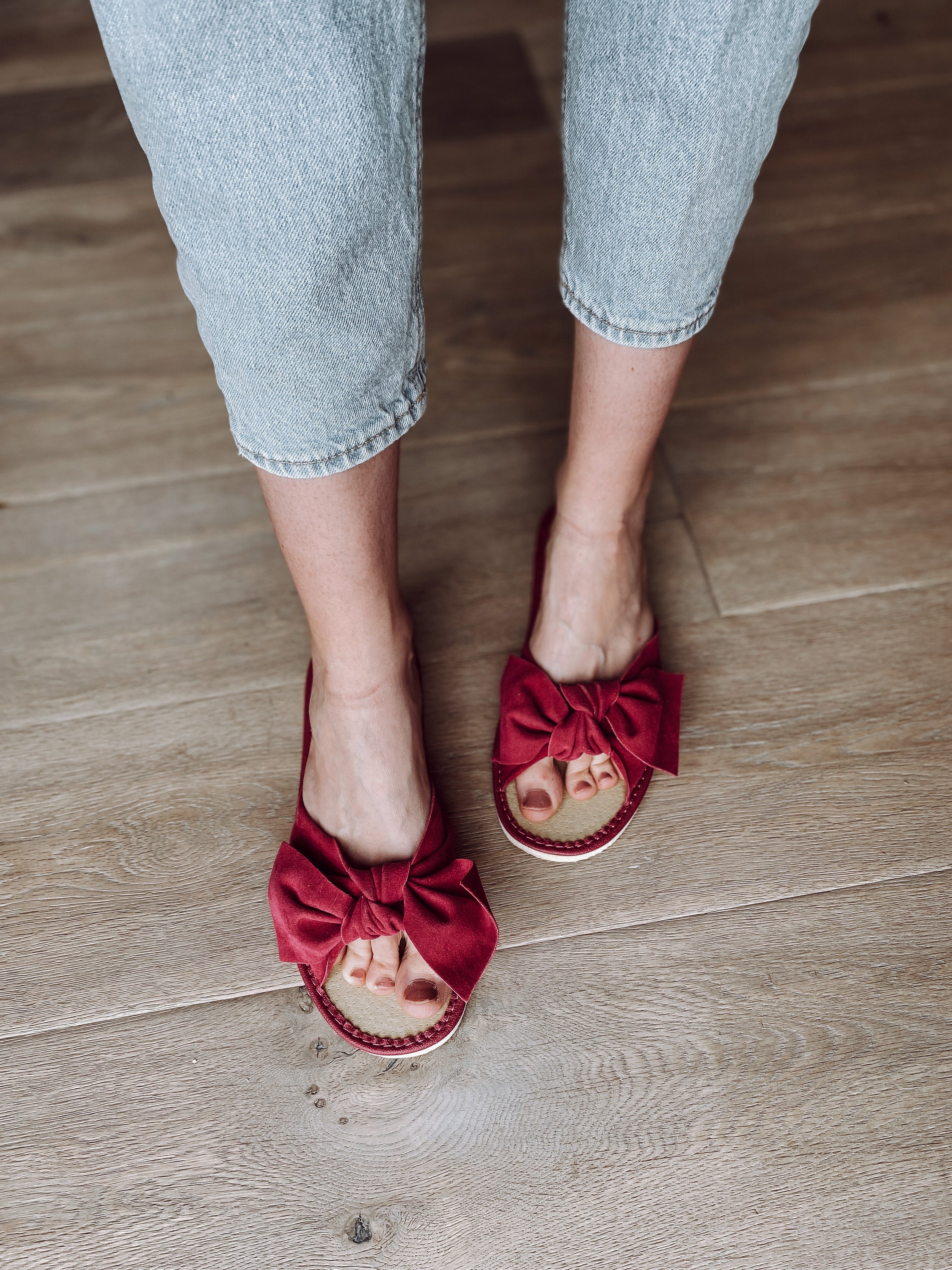 A pair of pink suede slippers featuring a decorative ribbon on the front, designed for comfort with a cushioned insole and foam bottom.