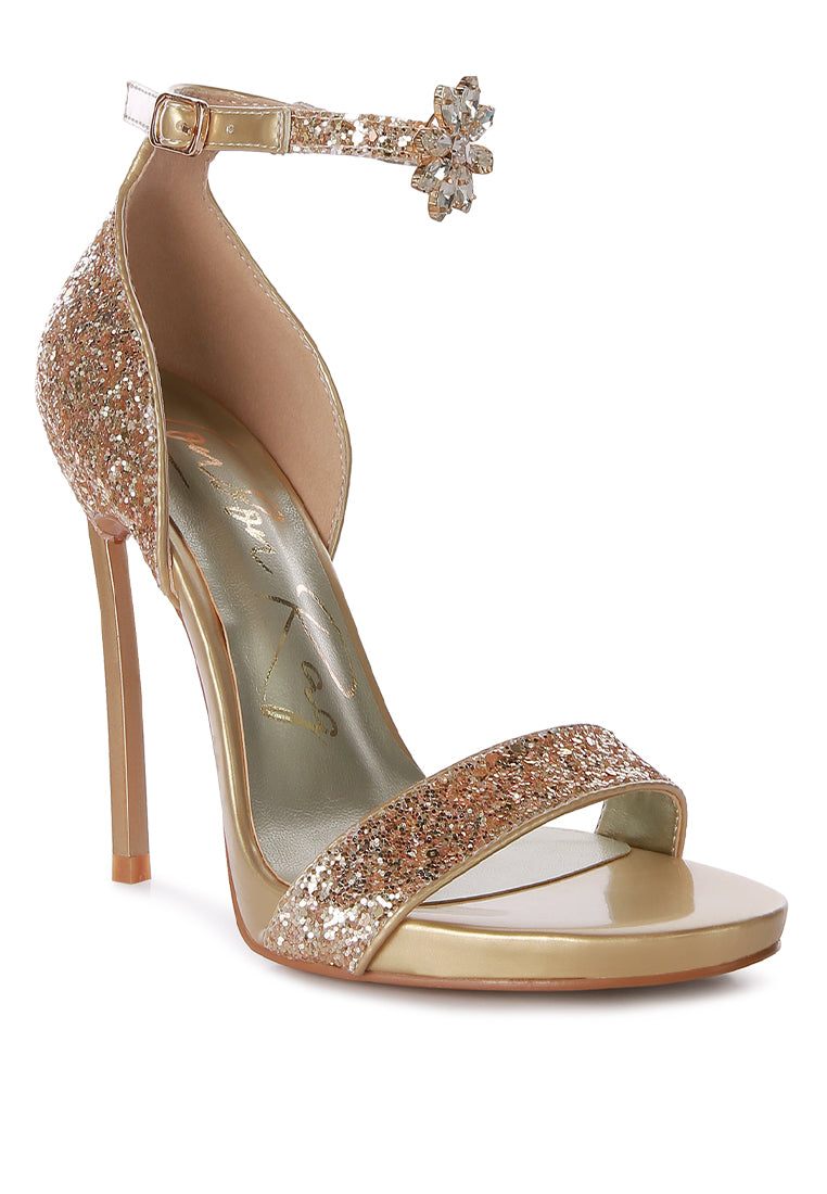 A pair of glamorous Straight Fire High Heel Glitter Stilettos featuring a glittery finish, floral jewel brooch, and a secure ankle strap.