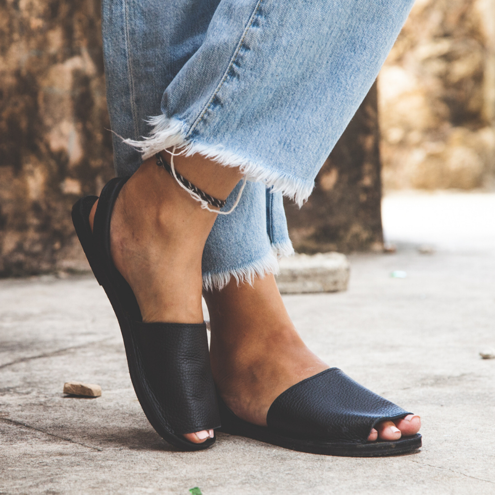 The Avarca women's flat leather sandal in black, showcasing its minimalist design and strappy heel.