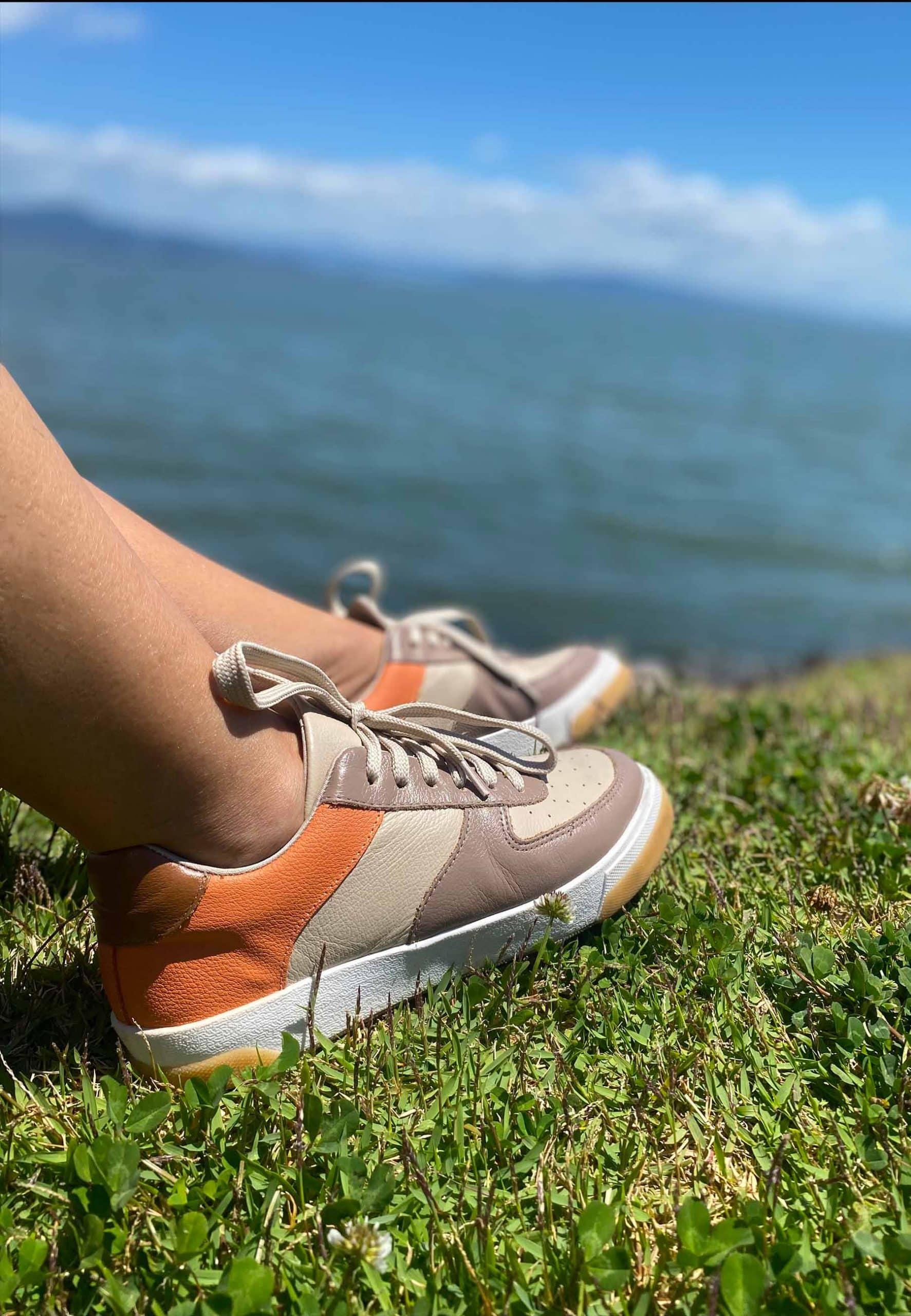 A pair of elegant women's sneakers in beige leather with brown and orange accents, featuring a lace-up front and padded collar.