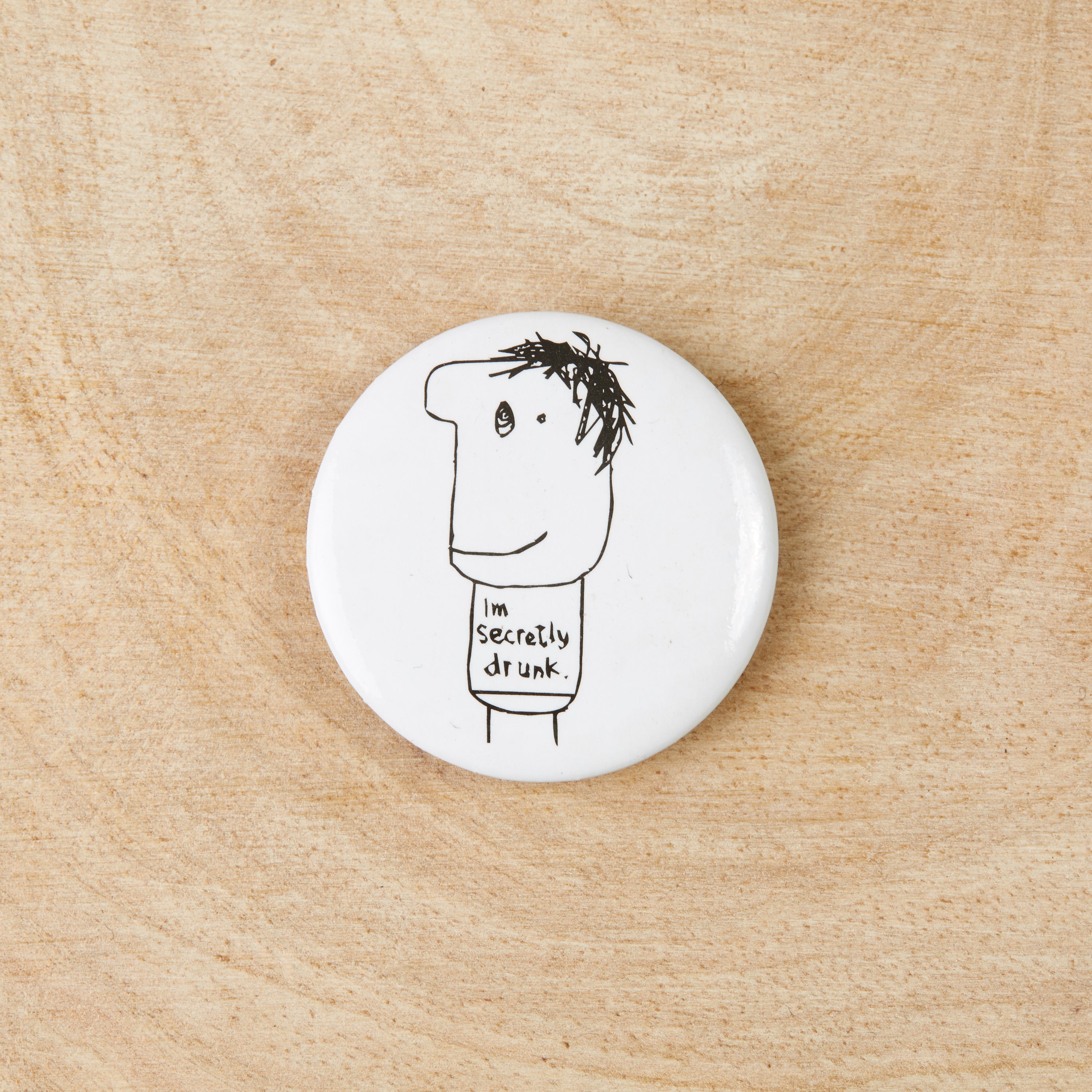 A stylish Secretly Drunk Badge featuring a black design on a white background, measuring 38mm in width, made from recycled materials.