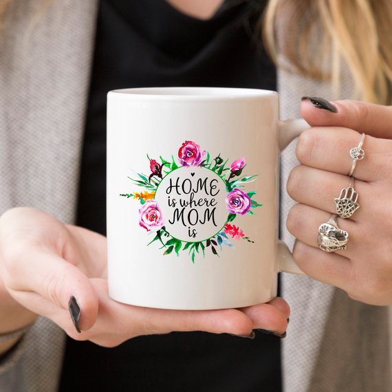 White 11oz coffee mug with funny design 'Home Is Where Mom Is' printed on both sides, showcasing high-quality ceramic material.