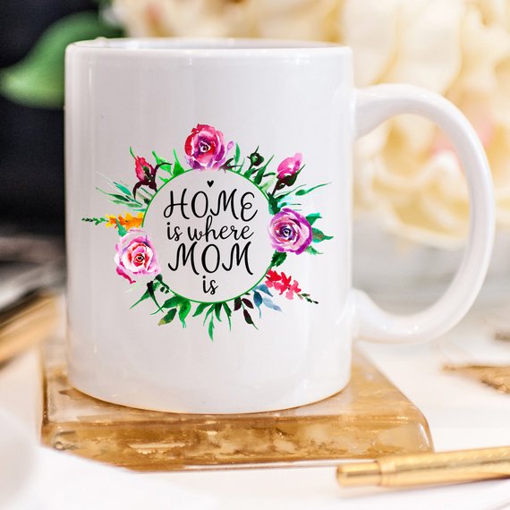 White 11oz coffee mug with funny design 'Home Is Where Mom Is' printed on both sides, showcasing high-quality ceramic material.