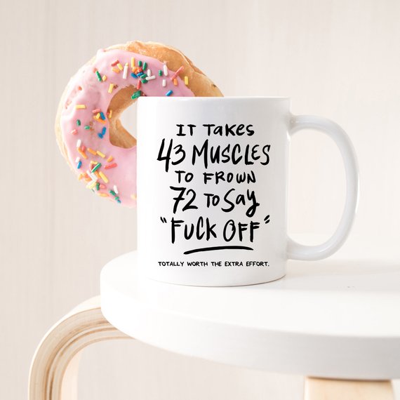 A humorous coffee mug featuring the phrase 'It Takes 43 Muscles To Frown, 72 To Say 'Fuck Off'.' Perfect for coffee lovers.