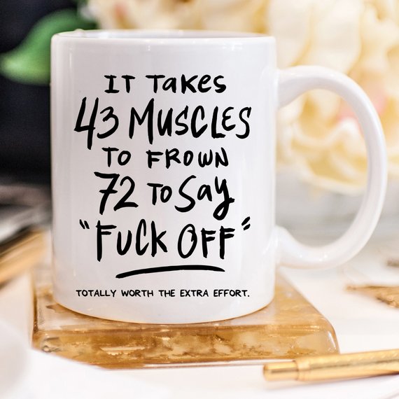 A humorous coffee mug featuring the phrase 'It Takes 43 Muscles To Frown, 72 To Say 'Fuck Off'.' Perfect for coffee lovers.