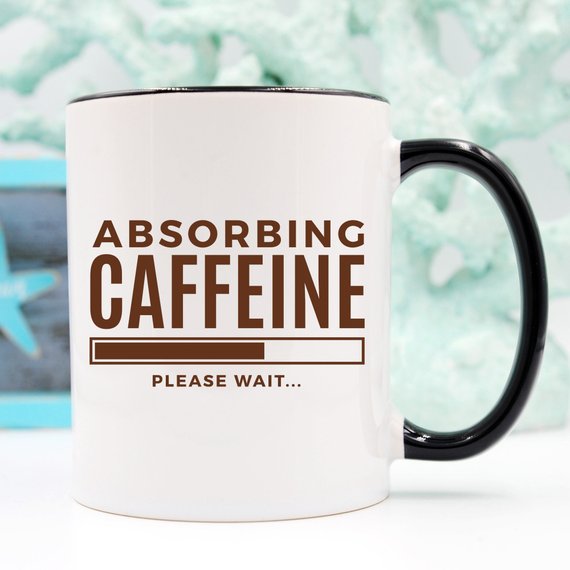 A humorous coffee mug with the phrase 'Absorbing Caffeine Please Wait', showcasing a fun design perfect for Mother's Day gifts.