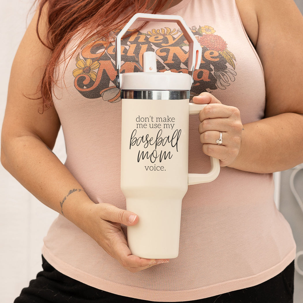 A stylish cream tumbler with a stainless steel interior, featuring the phrase 'Don't Make Me Use My Baseball Mom Voice' in bold black graphic.