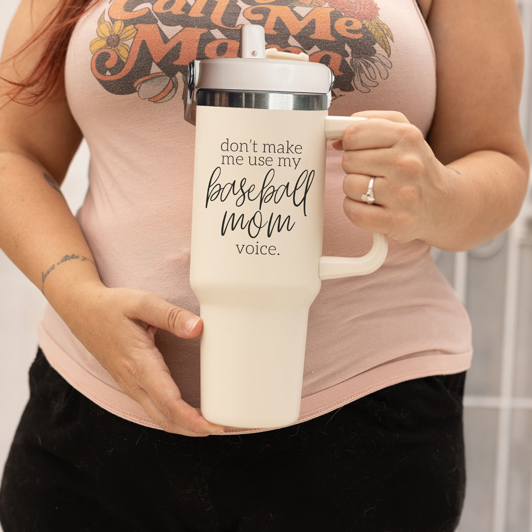 A stylish cream tumbler with a stainless steel interior, featuring the phrase 'Don't Make Me Use My Baseball Mom Voice' in bold black graphic.