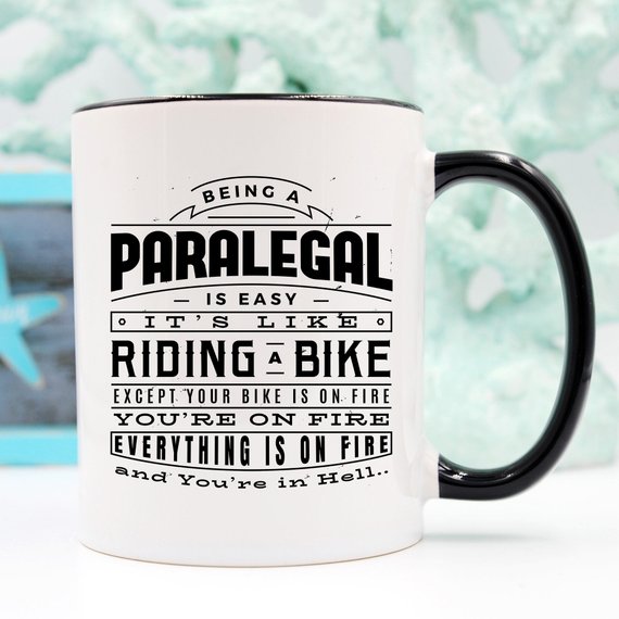 A humorous coffee mug featuring the phrase 'Being A Paralegal Is Easy' with a fiery design, perfect for paralegals.