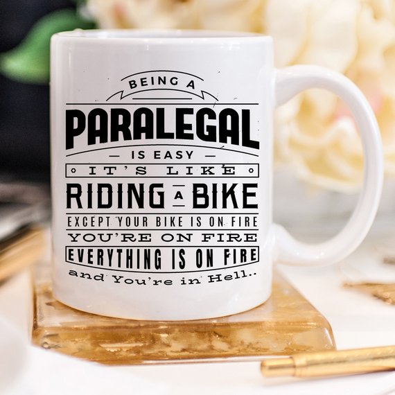 A humorous coffee mug featuring the phrase 'Being A Paralegal Is Easy' with a fiery design, perfect for paralegals.