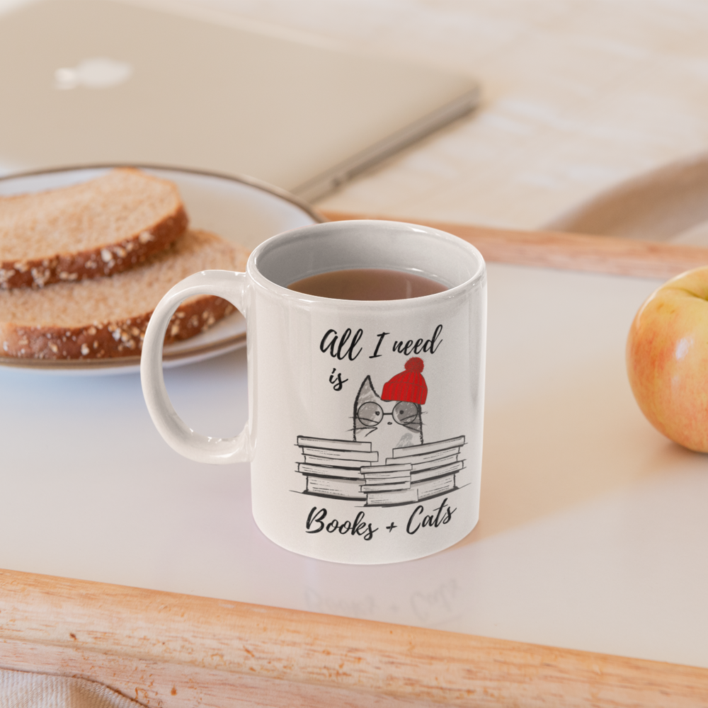 A white ceramic mug with the phrase 'All I Need is Books & Cats' printed on it, perfect for book lovers.