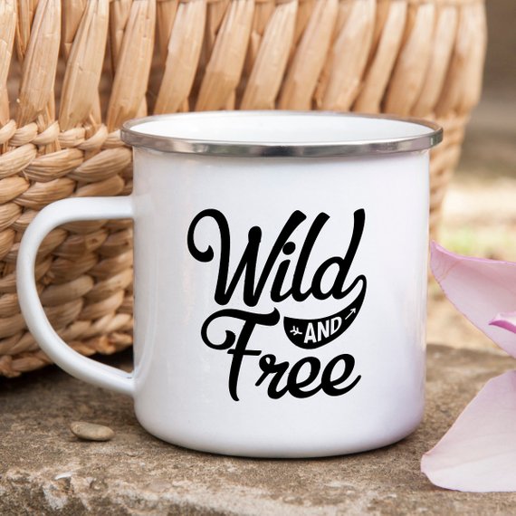 White enamel camping mug with stainless steel rim featuring 'Wild and Free' design on both sides, perfect for outdoor adventures.