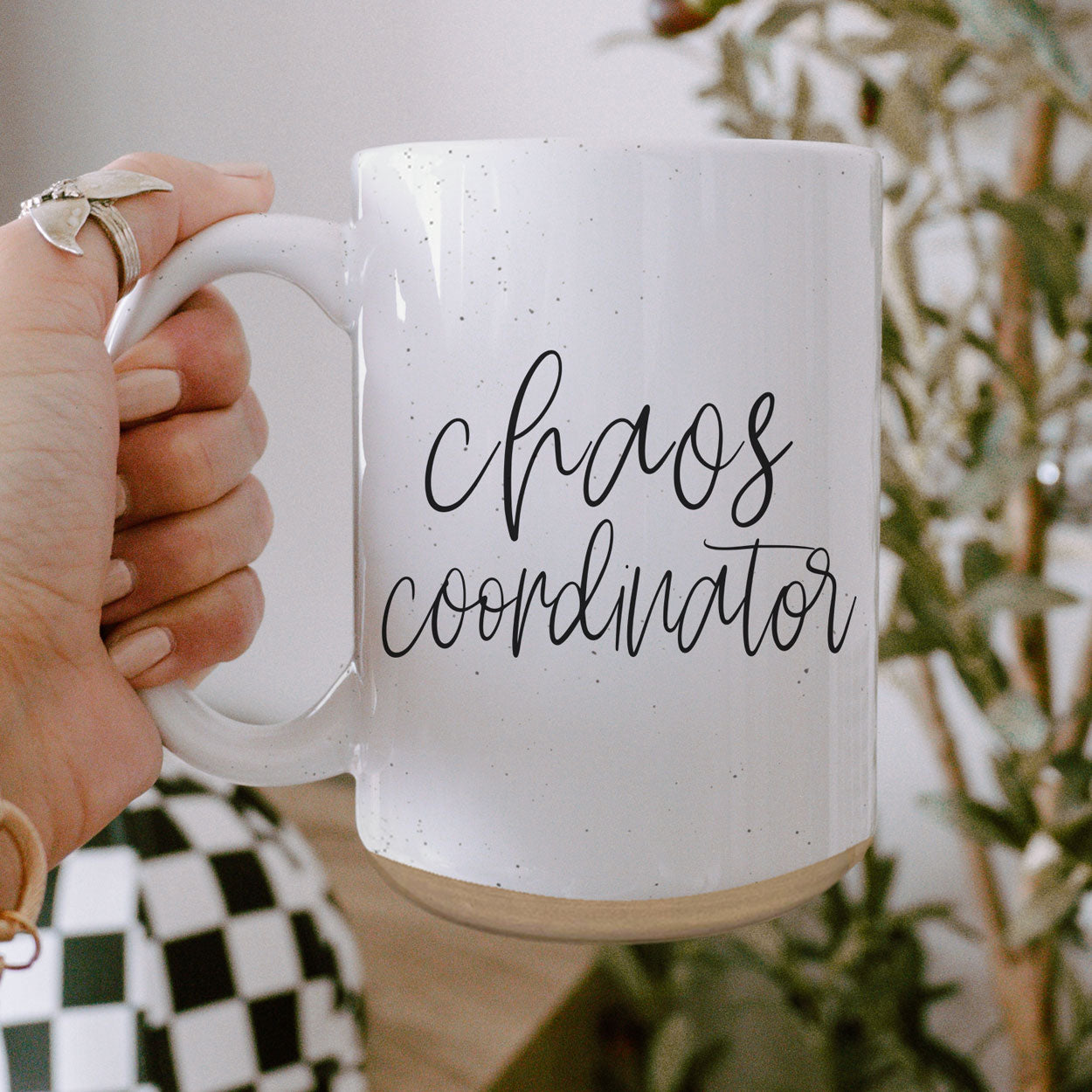 A humorous 'Chaos Coordinator' 16oz coffee mug featuring a black graphic on an off-white ceramic body with dark speckles.