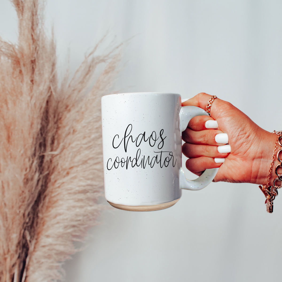 A humorous 'Chaos Coordinator' 16oz coffee mug featuring a black graphic on an off-white ceramic body with dark speckles.