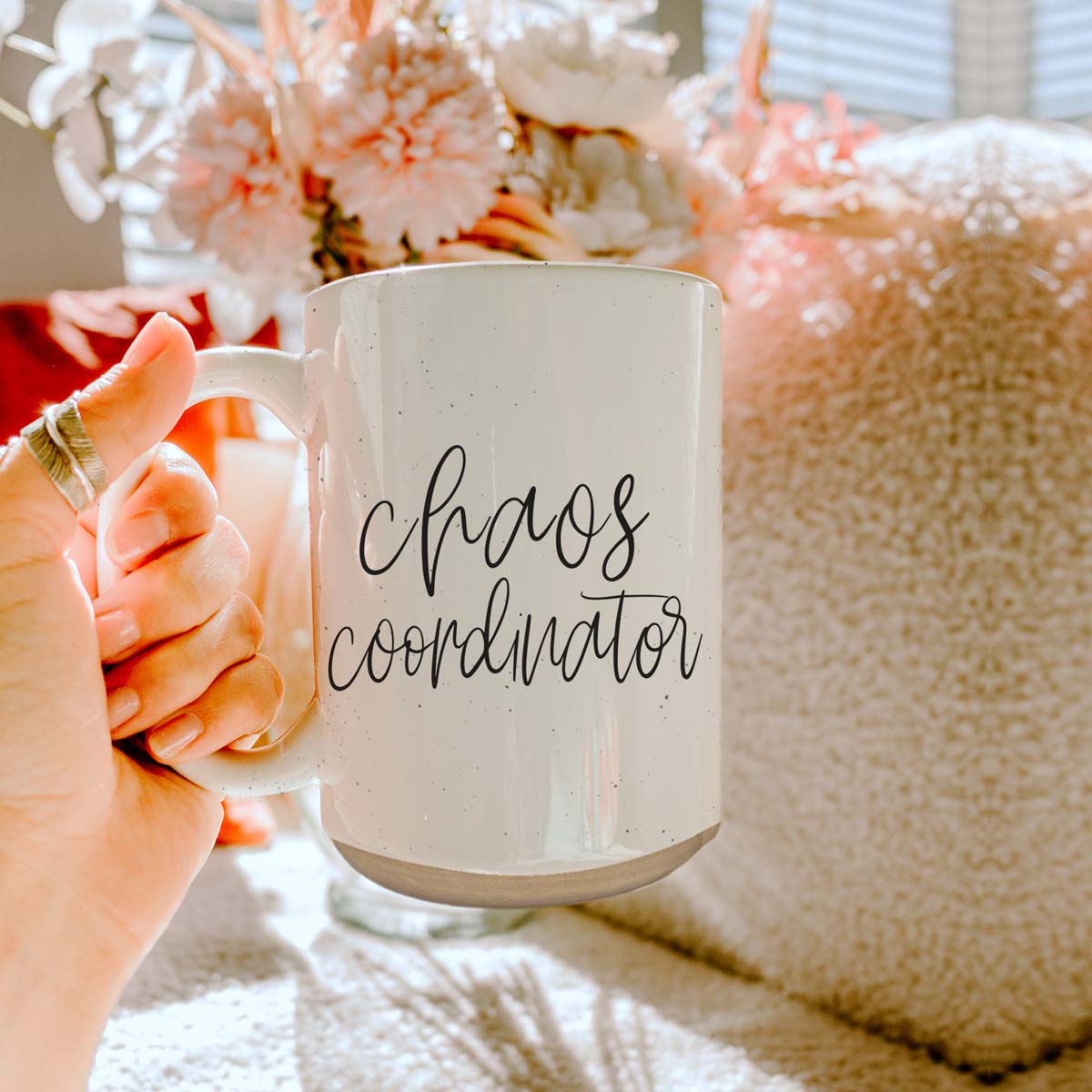 A humorous 'Chaos Coordinator' 16oz coffee mug featuring a black graphic on an off-white ceramic body with dark speckles.