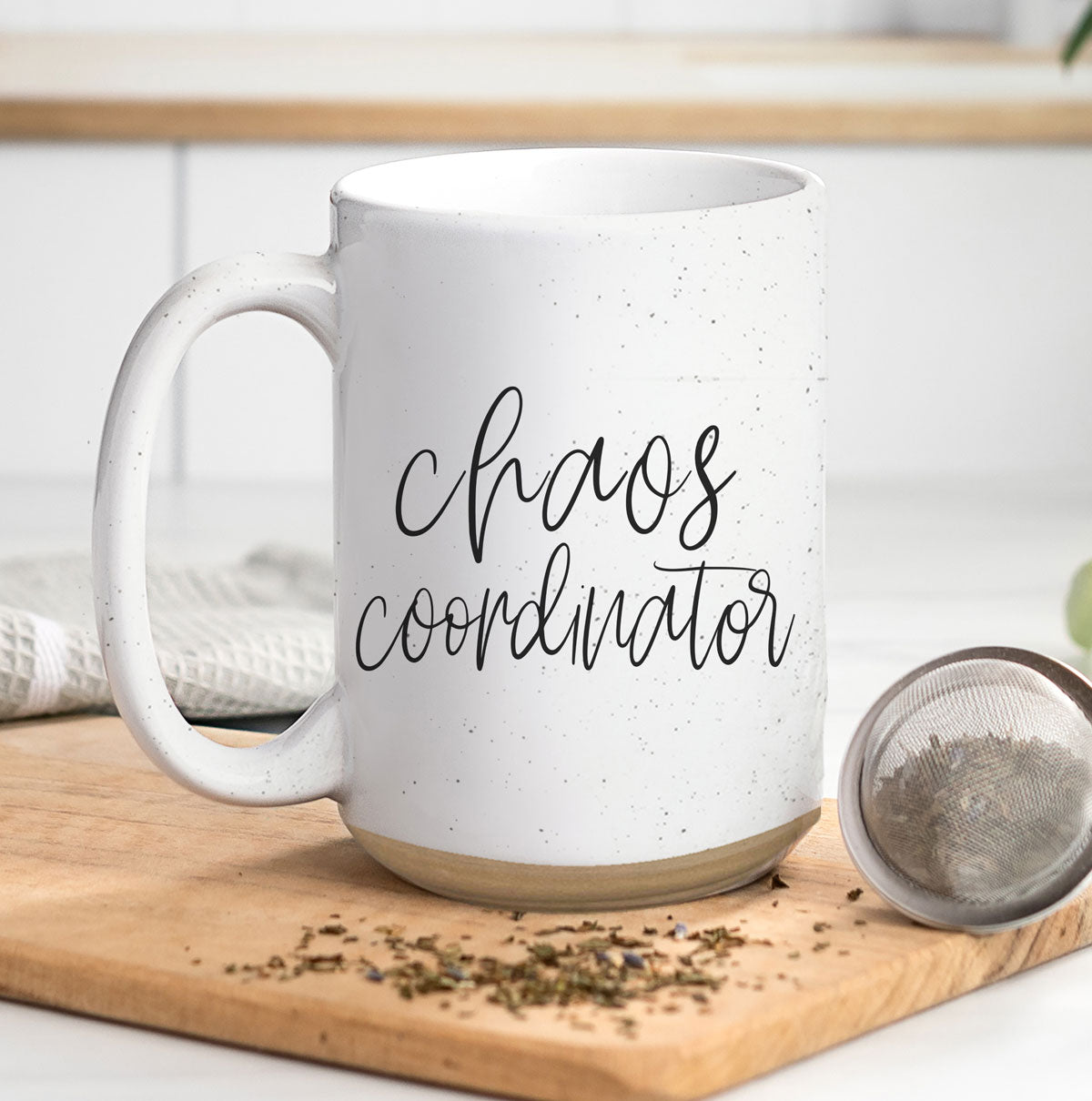 A humorous 'Chaos Coordinator' 16oz coffee mug featuring a black graphic on an off-white ceramic body with dark speckles.