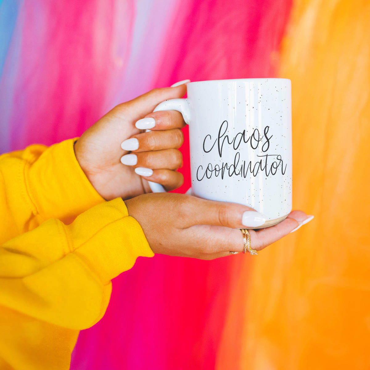 A humorous 'Chaos Coordinator' 16oz coffee mug featuring a black graphic on an off-white ceramic body with dark speckles.