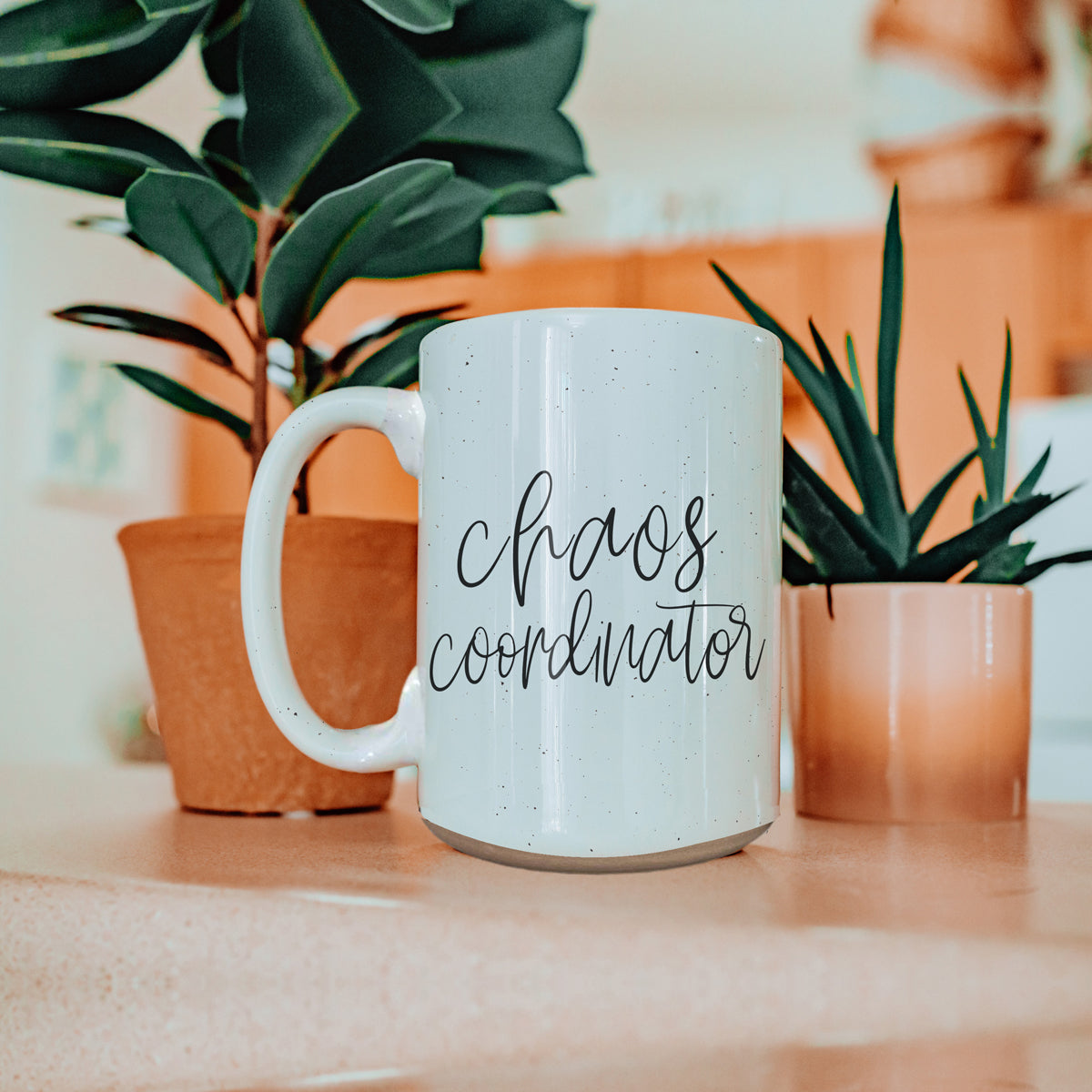 A humorous 'Chaos Coordinator' 16oz coffee mug featuring a black graphic on an off-white ceramic body with dark speckles.