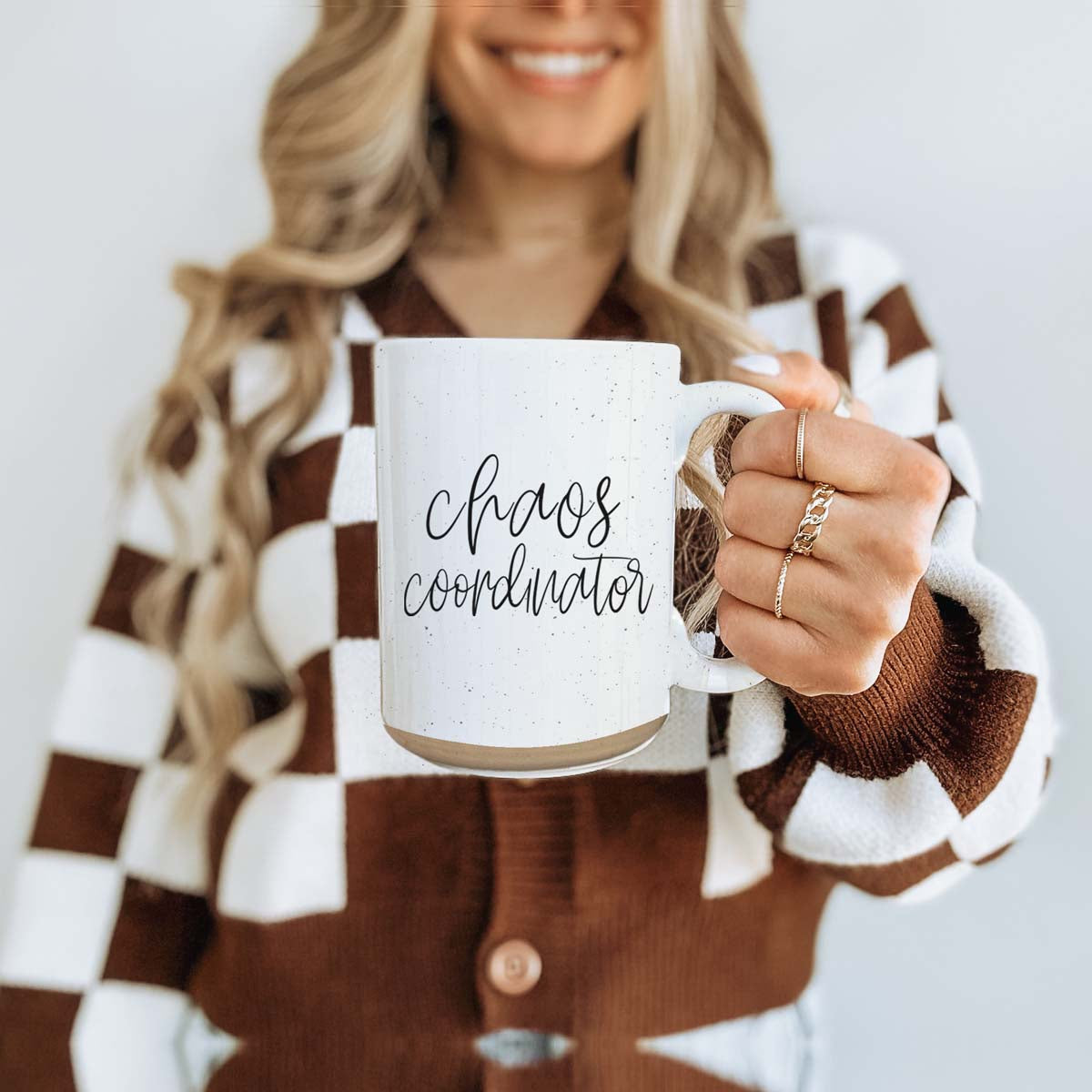 A humorous 'Chaos Coordinator' 16oz coffee mug featuring a black graphic on an off-white ceramic body with dark speckles.