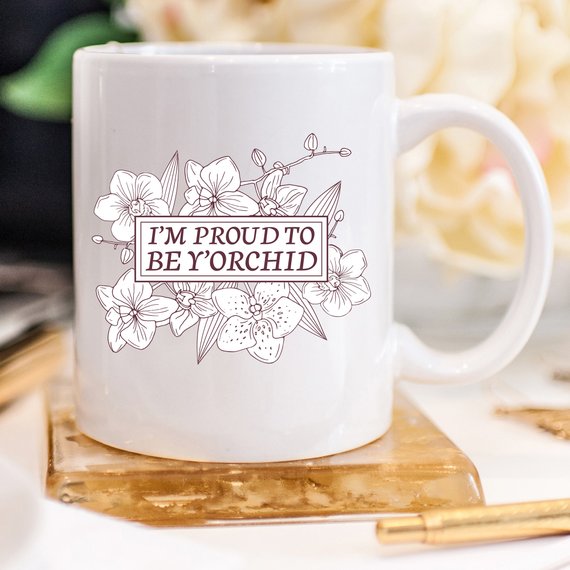 A humorous coffee mug with the phrase 'I'm Proud To Be Y'orchid', showcasing a vibrant design perfect for gifting.