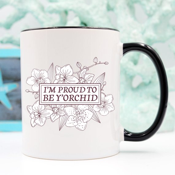 A humorous coffee mug with the phrase 'I'm Proud To Be Y'orchid', showcasing a vibrant design perfect for gifting.