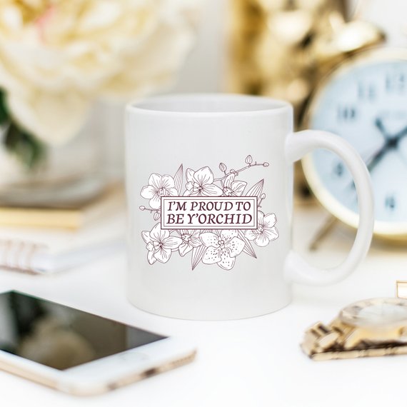 A humorous coffee mug with the phrase 'I'm Proud To Be Y'orchid', showcasing a vibrant design perfect for gifting.