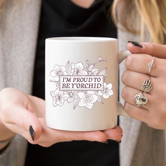 A humorous coffee mug with the phrase 'I'm Proud To Be Y'orchid', showcasing a vibrant design perfect for gifting.