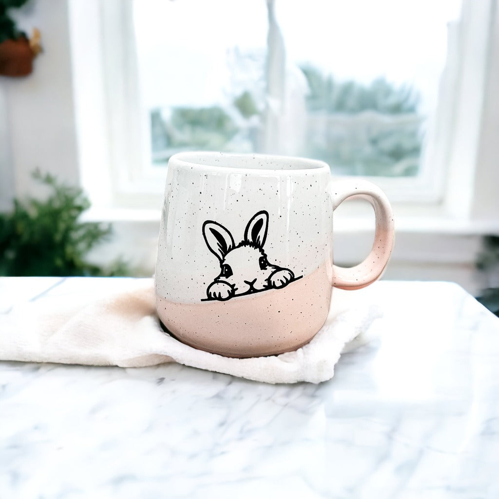 Handcrafted ceramic mug featuring a bunny silhouette and pastel pink base, perfect for coffee or tea.