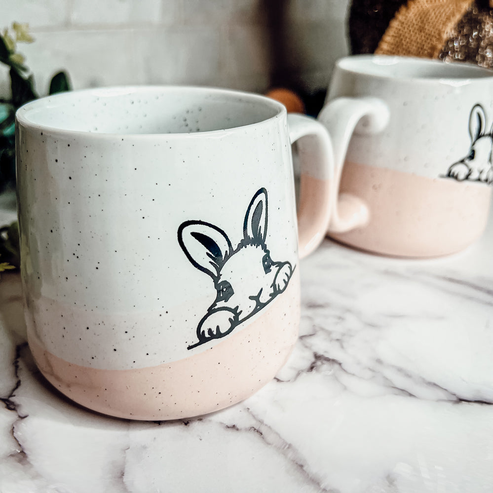 Handcrafted ceramic mug featuring a bunny silhouette and pastel pink base, perfect for coffee or tea.