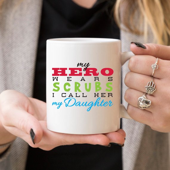 Funny Nurse Mug featuring the phrase 'My Hero Wears Scrubs, I Call Her My Daughter', perfect for coffee lovers.