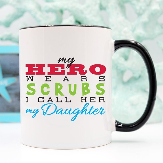 Funny Nurse Mug featuring the phrase 'My Hero Wears Scrubs, I Call Her My Daughter', perfect for coffee lovers.