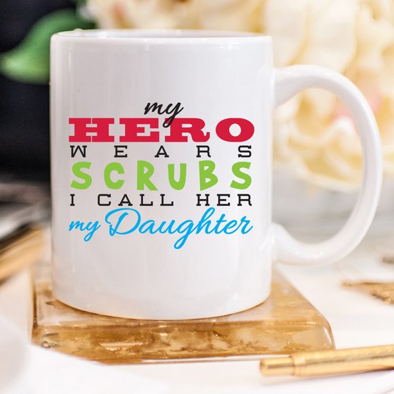 Funny Nurse Mug featuring the phrase 'My Hero Wears Scrubs, I Call Her My Daughter', perfect for coffee lovers.